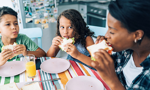 Woman and two children sitting at a table eating sandwiches.