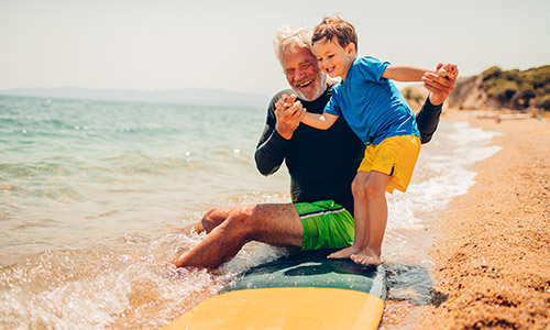 Older man and a child playing on the sand by the water's edge on the beach.